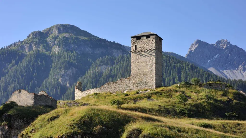 Medieval stone tower with mountain landscape in the background, Swiss Alps scenery.