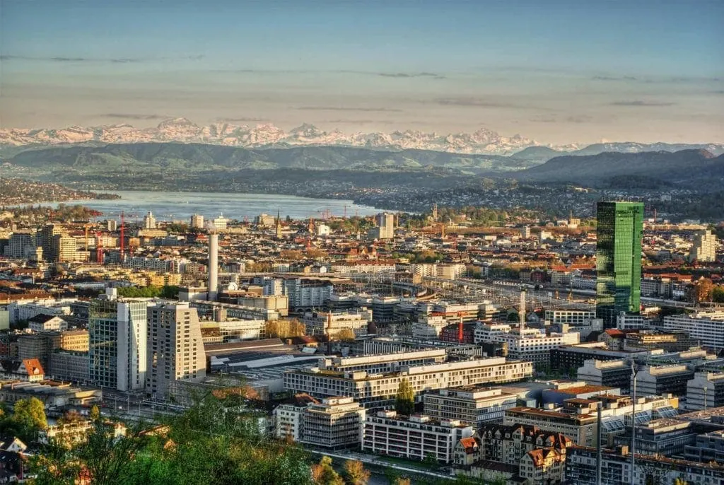 Modern Zurich cityscape with Lake Zurich and Swiss Alps in the background.