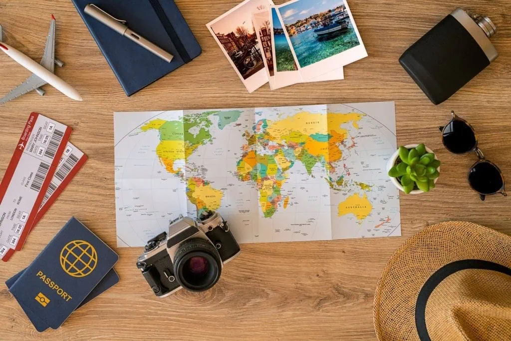 Colorful world map on wooden desk with travel accessories and souvenirs for travel planning.