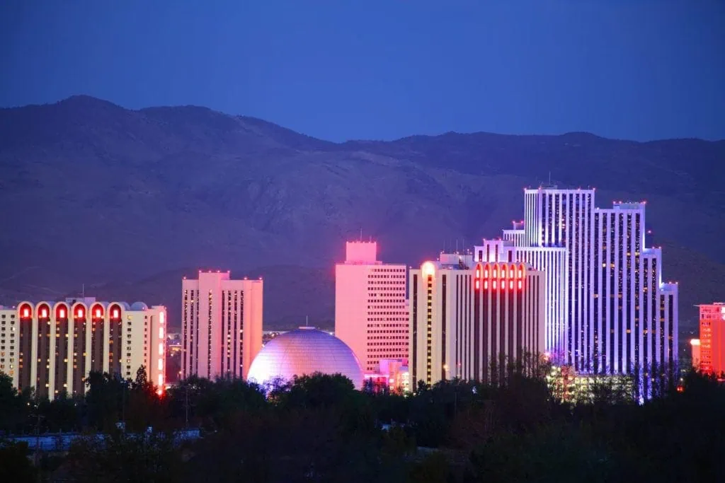 Bright city skyline with illuminated modern buildings against mountain backdrop.