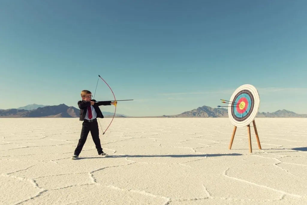 Archery boy aiming at target in outdoor desert landscape.
