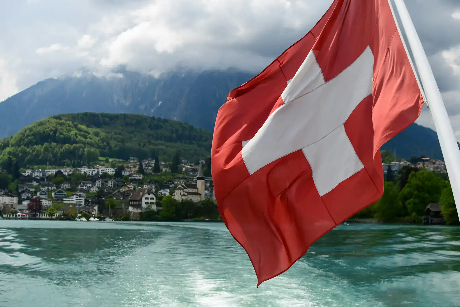 Switzerland lake view with Swiss flag, mountains and clear sky.
