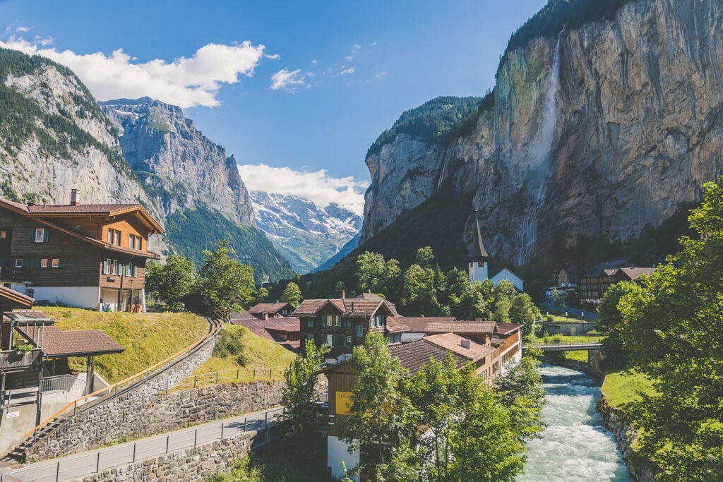 Traditional Swiss alpine village with wooden chalets and a river beneath steep valley cliffs.