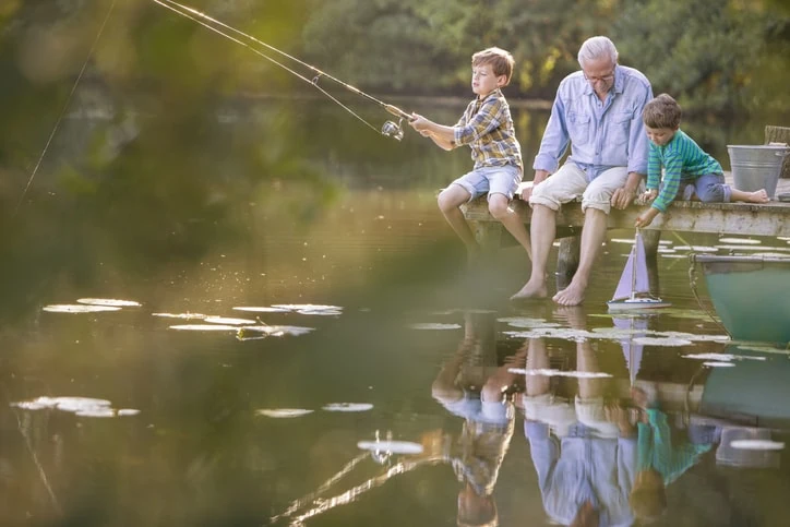 Grandfather sitting with grandchildren near a lake and they fish