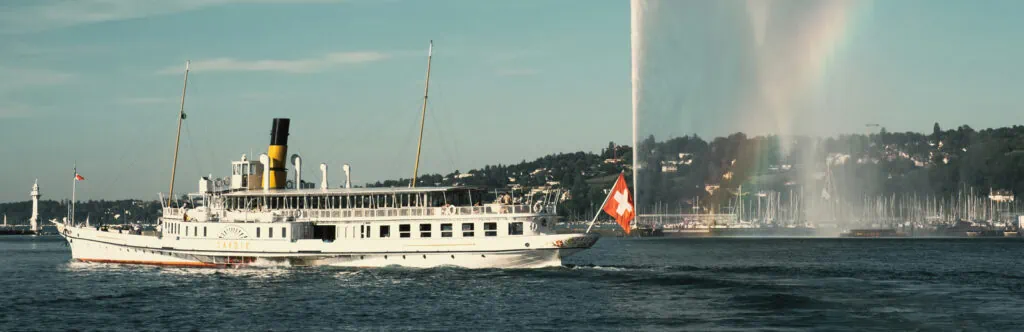 Classic Swiss boat sailing on Lake Geneva with mountains in background.