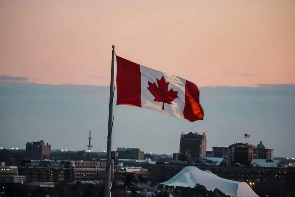 Canadian flag flying in cityscape at sunset.