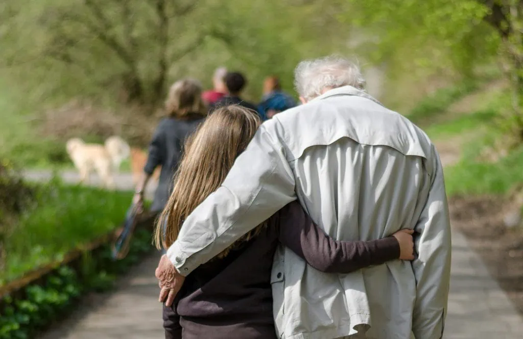 Compassionate elderly man walking with young girl in nature, caring and supportive scene.