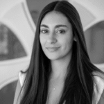 Professional woman with long dark hair smiling in modern office setting.