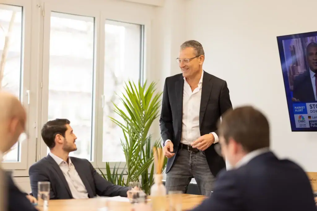 In a bright modern conference room, a man is explaining something to colleagues