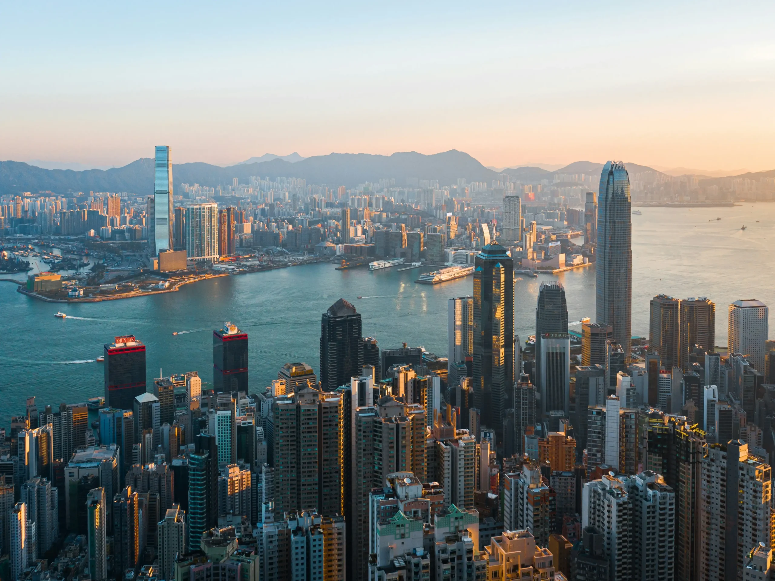 Aerial view of Hong Kong skyline at sunset with skyscrapers and Victoria Harbour.