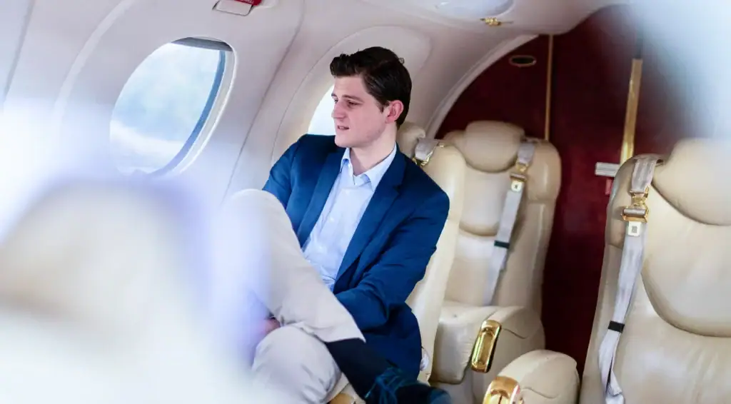 Young businessman sitting in private jet cabin, looking out window.