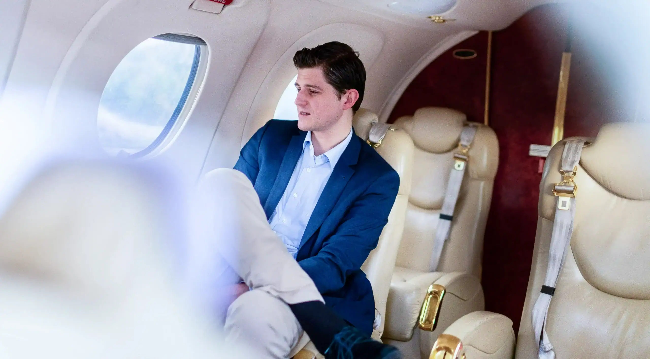 Young businessman sitting in private jet cabin, looking out window.