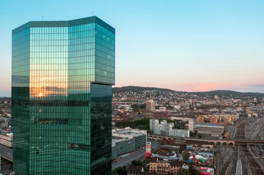 Contemporary glass office tower reflecting sunset in Zurich skyline.