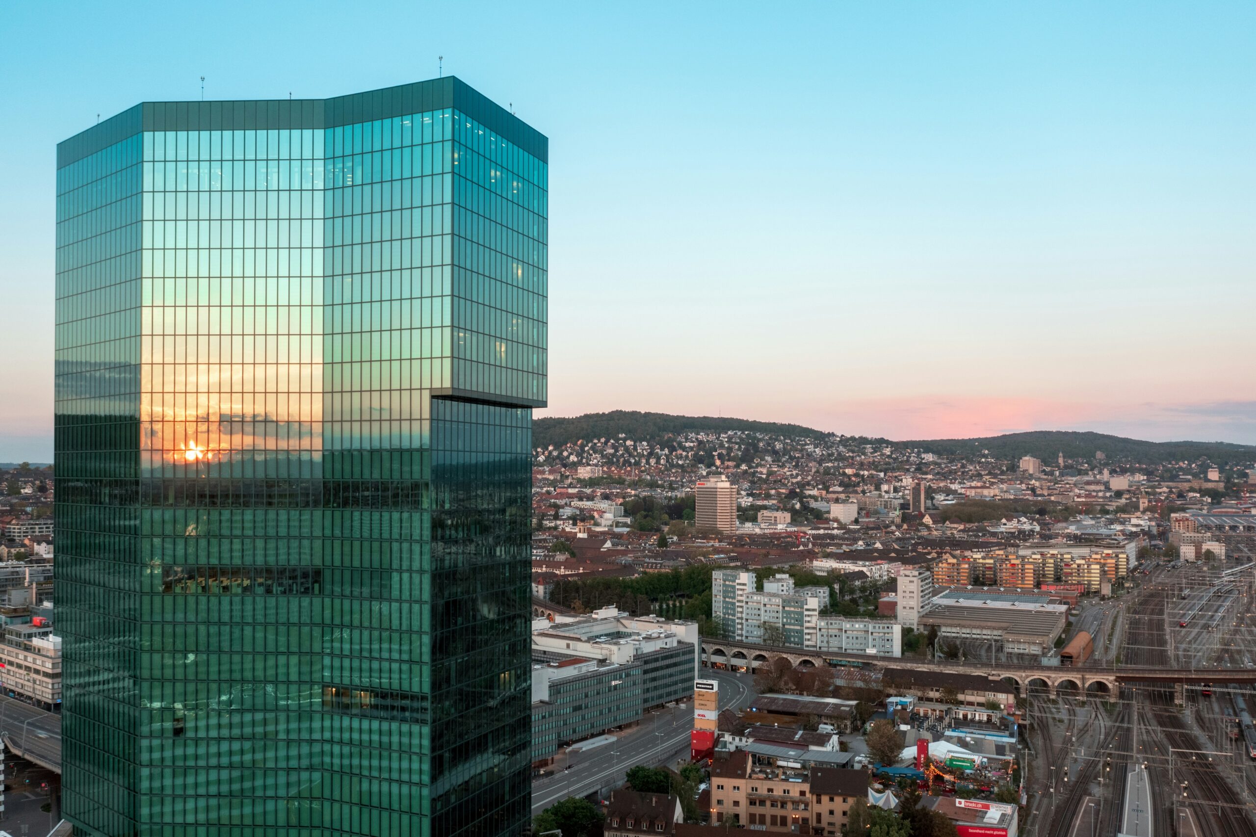 Contemporary glass office tower reflecting sunset in Zurich skyline.