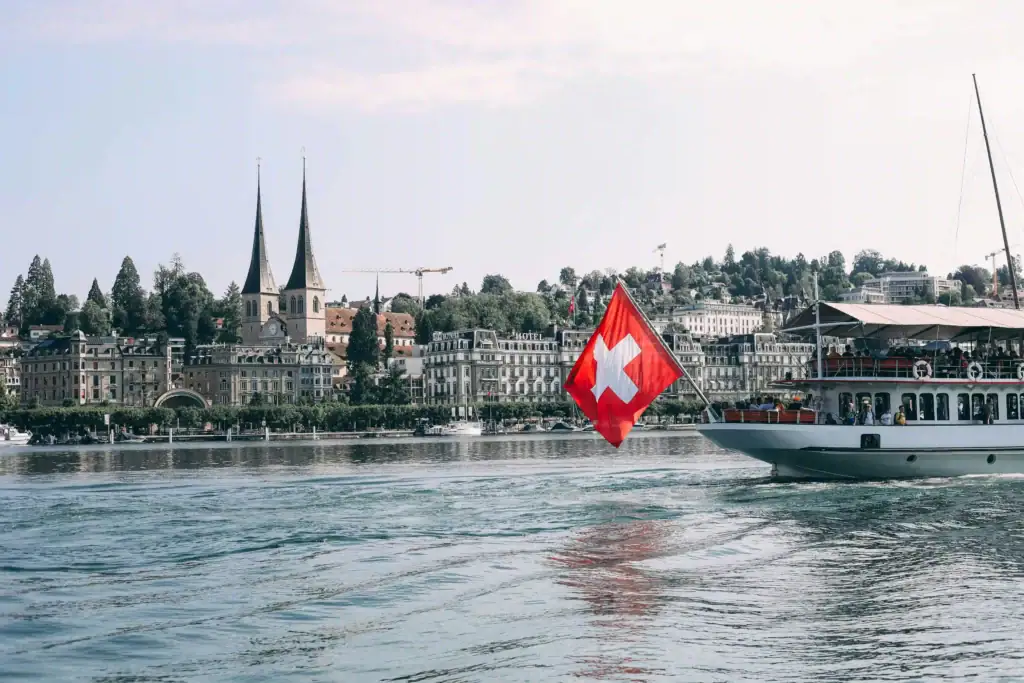 Switzerland flag on boat in Lake Zurich with city and church spires in background.