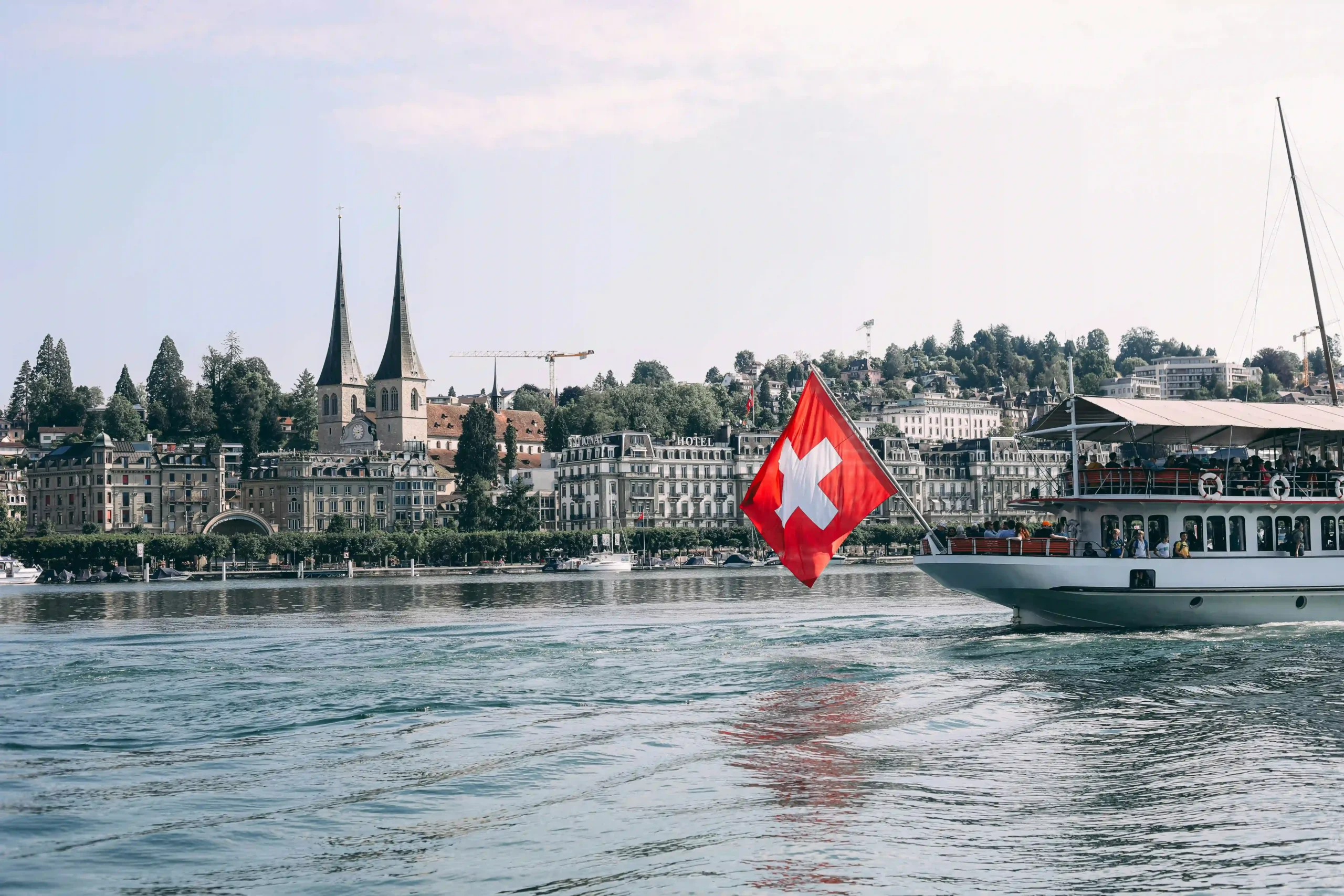 Switzerland flag on boat in Lake Zurich with city and church spires in background.