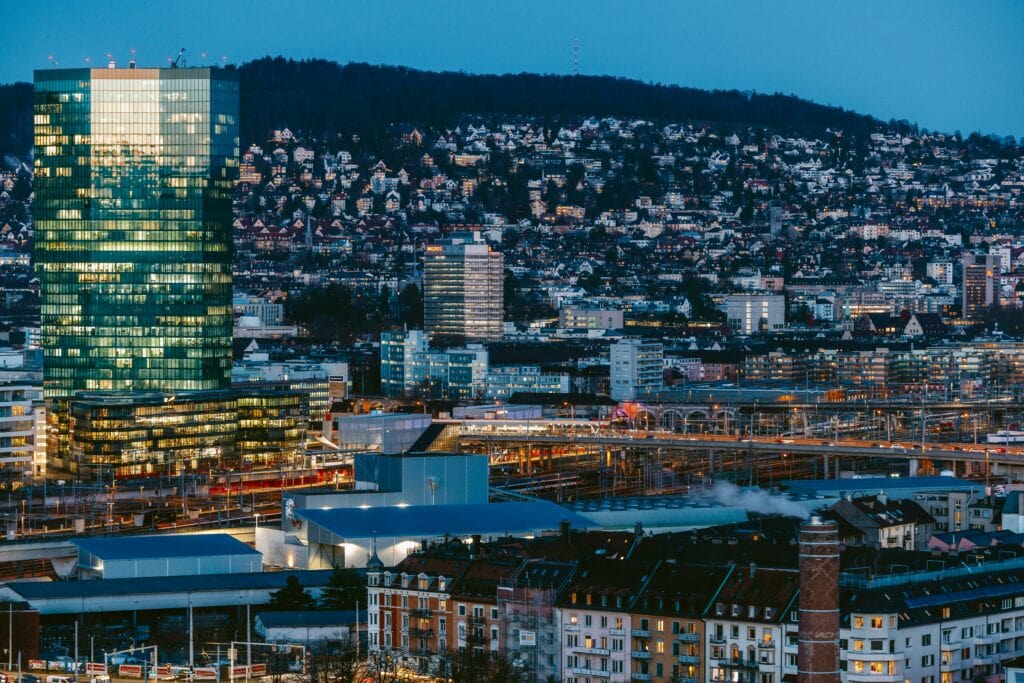 Night view of Zurich city with modern buildings and hills in background.